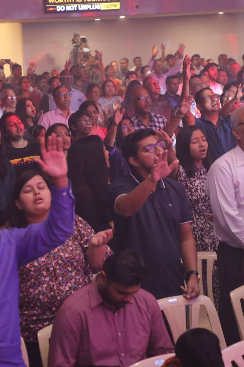 Indian congregation lifting their hands and worshiping fervently in City Harvest Church.