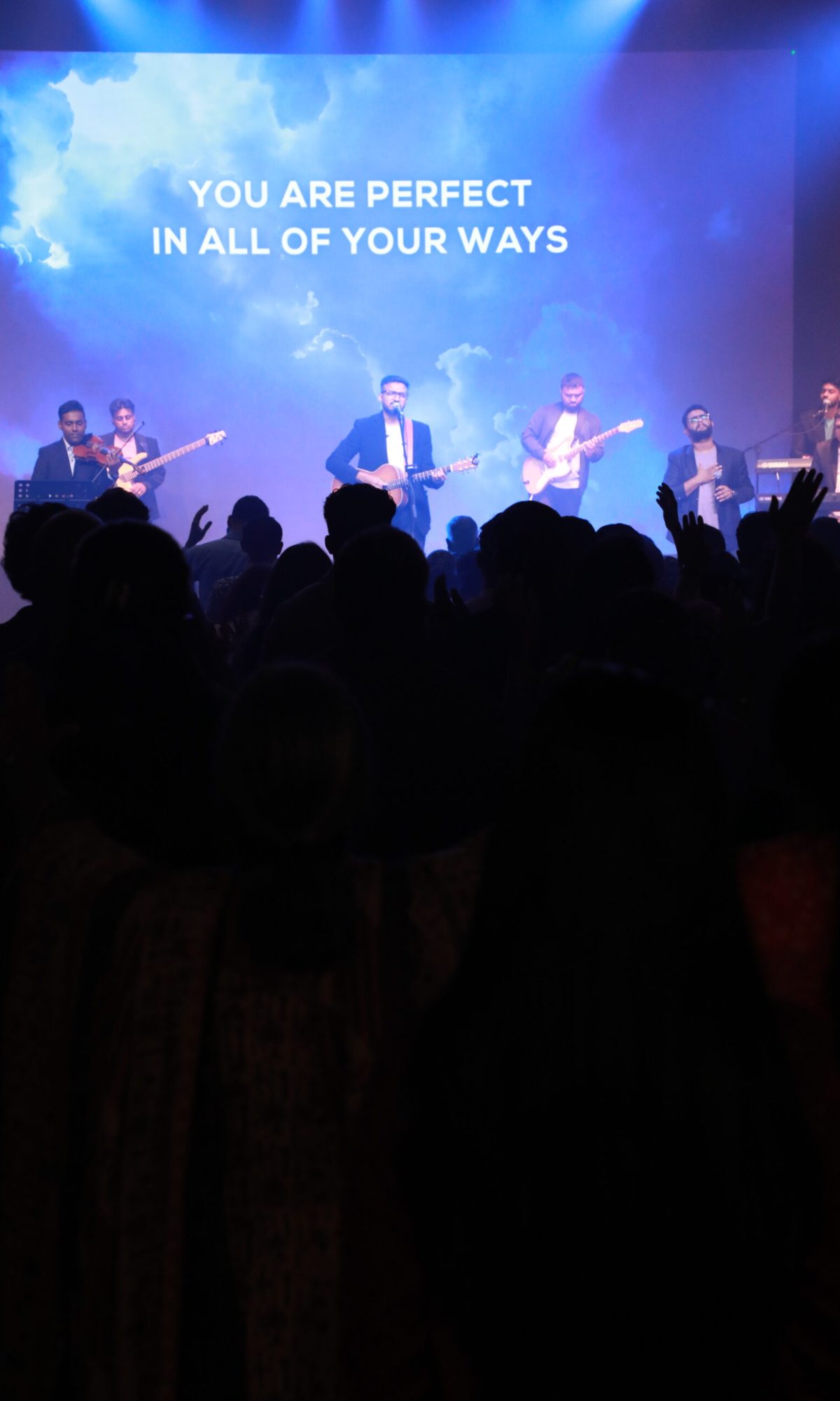 Worship leader and musicians leading the praise and worship session in front of a blue background.